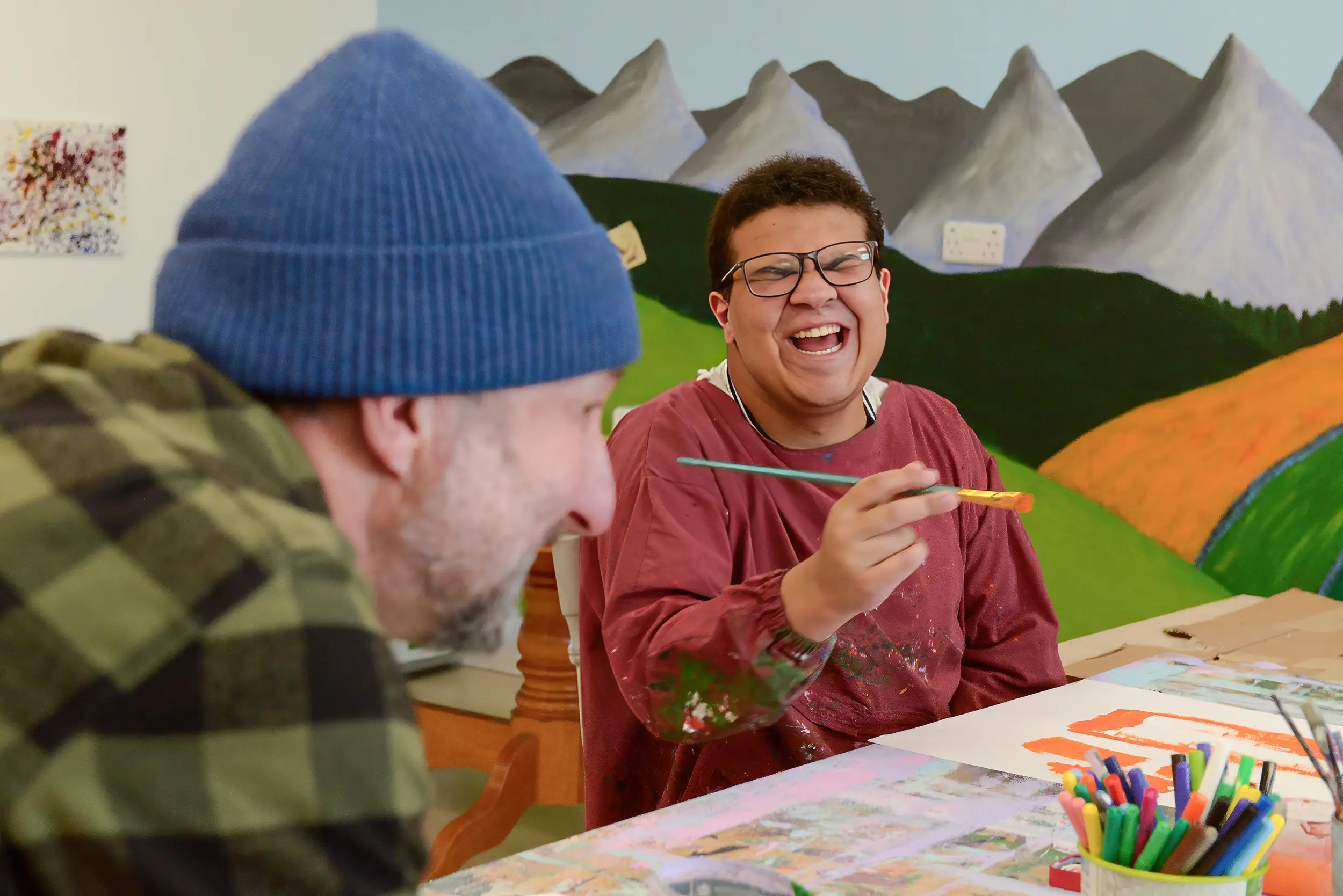 Young man laughing while painting with a staff member